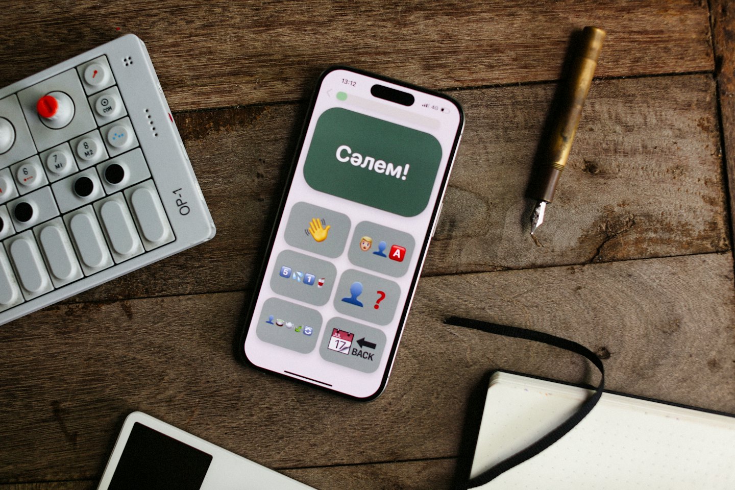 Smartphone with emojis sits on a wooden desk near a synthesizer.